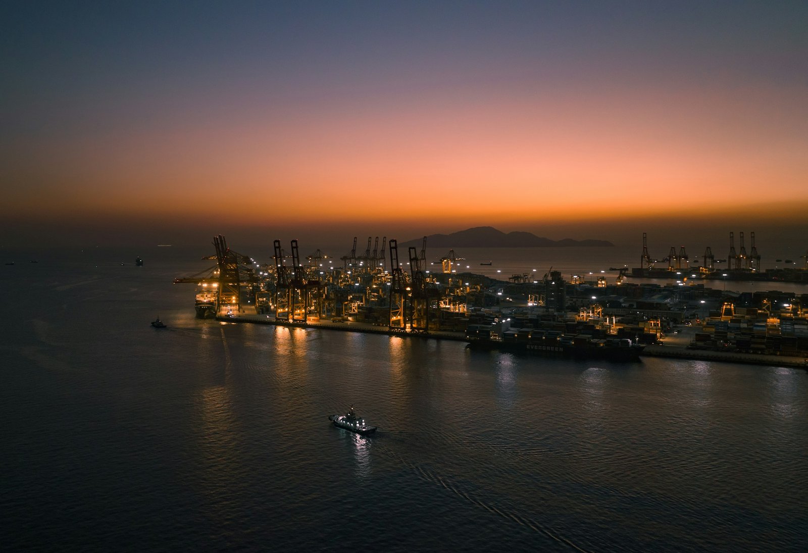A working harbour at dusk with container cranes and a small boat on the water