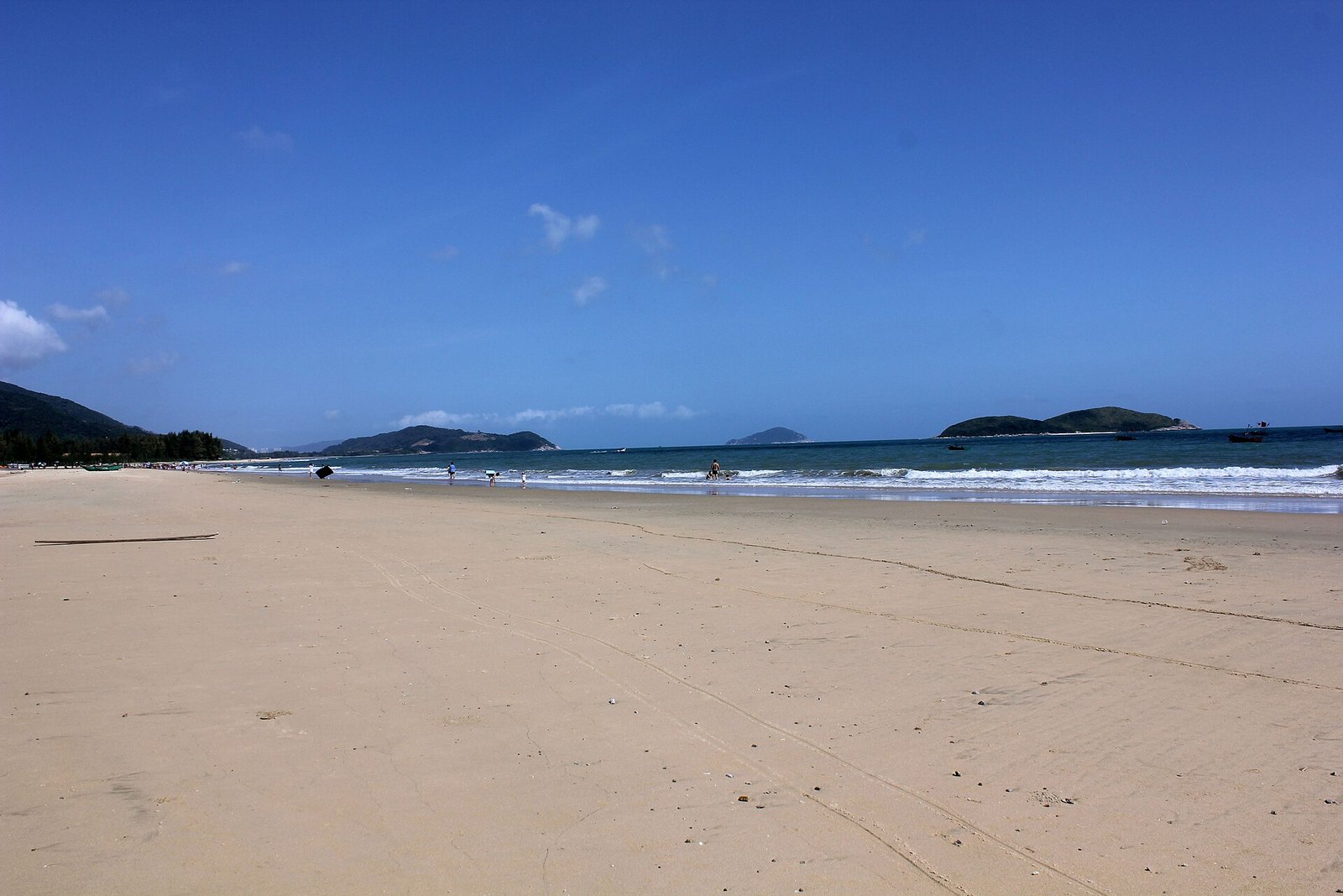 A wide empty beach at Shimei Bay in Wanning with low green hills on the horizon