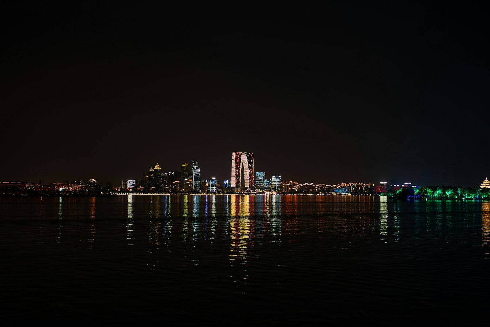 A modern city skyline of glass towers reflected in a lake at dusk