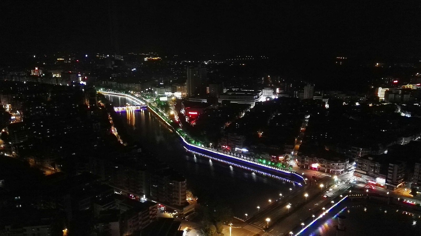 A city skyline at night seen from a tower, with lit streets, apartment blocks and a river
