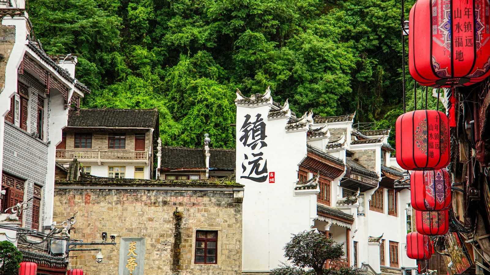 A traditional Chinese village of old houses with red lanterns and green mountains behind
