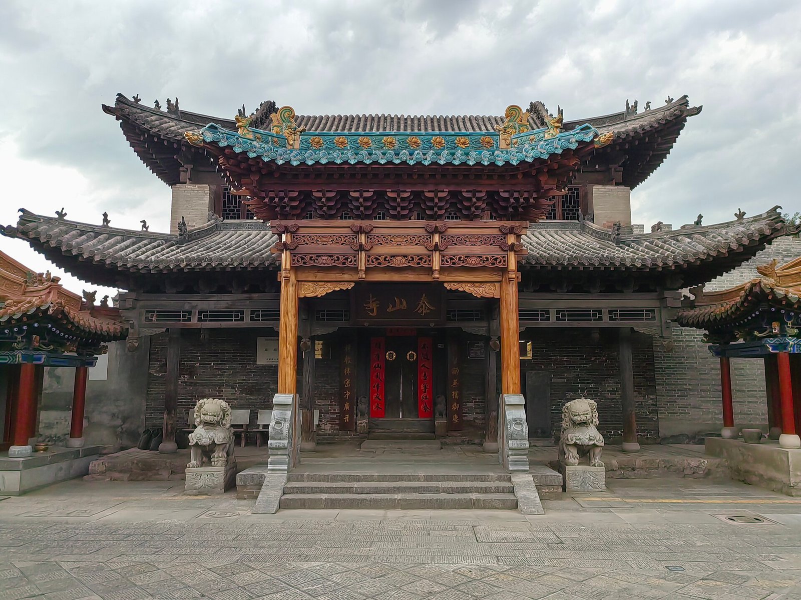 A temple gate with red columns, a green glazed tile roof and painted beams, with stone steps in front