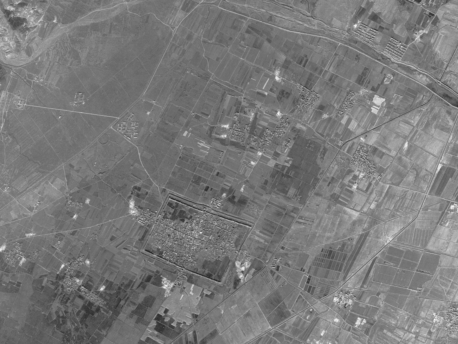 A grainy black and white satellite photograph of a river valley, with built-up ground and surrounding fields