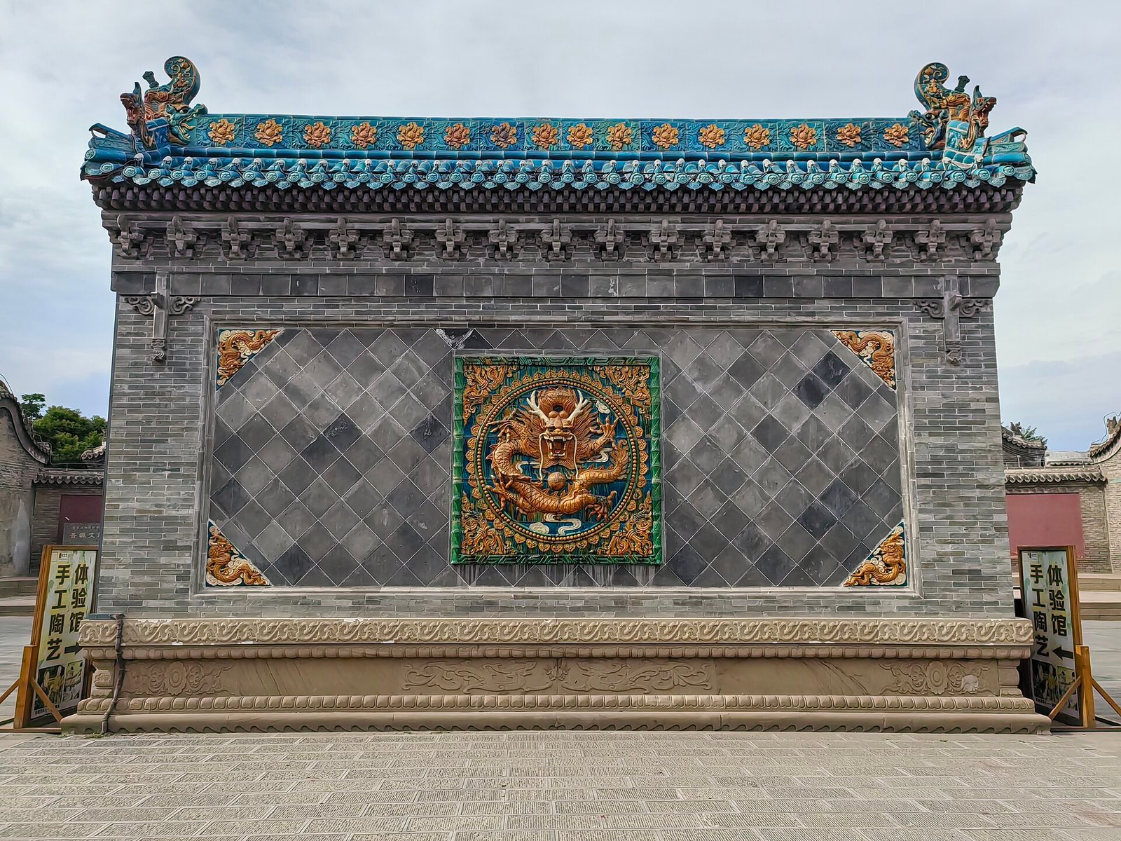 A glazed tile screen wall with a central circular panel, standing in front of a temple courtyard