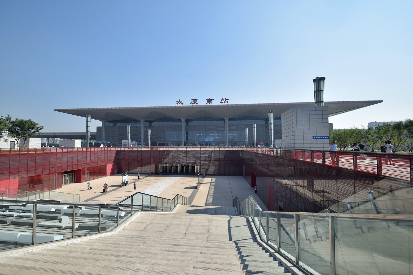 A large modern railway station with a wide roof and a glass facade, seen from the square in front