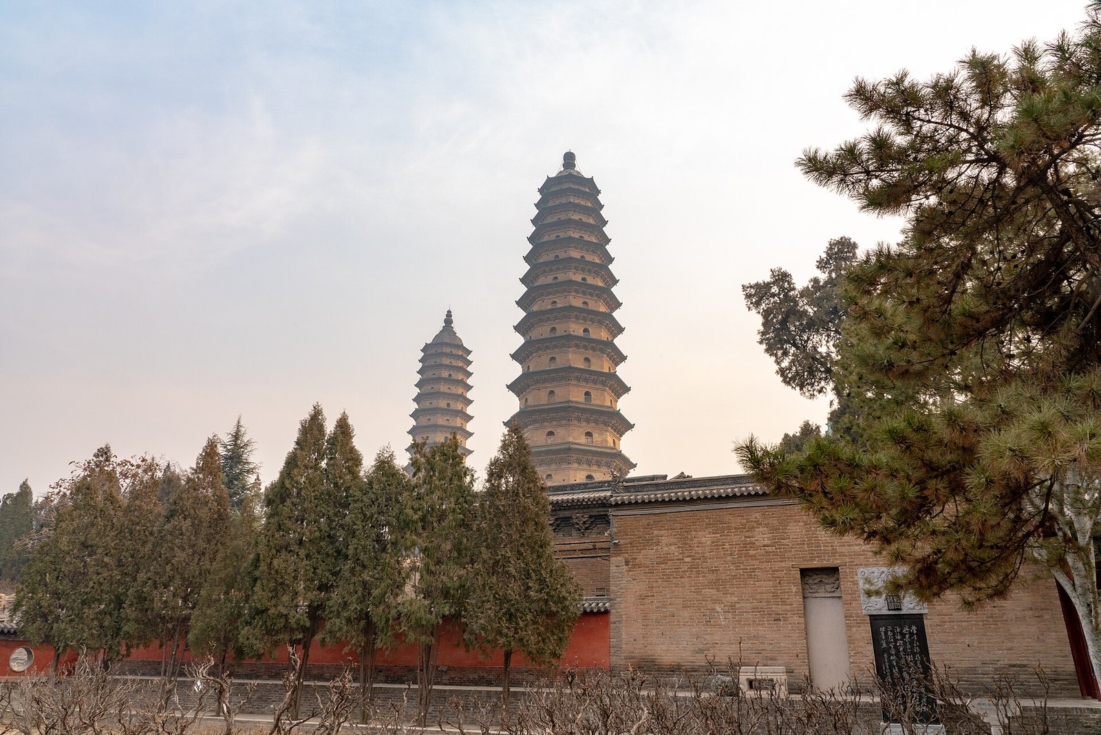 Two tall brick pagodas of thirteen storeys each, rising above a temple roof and trees