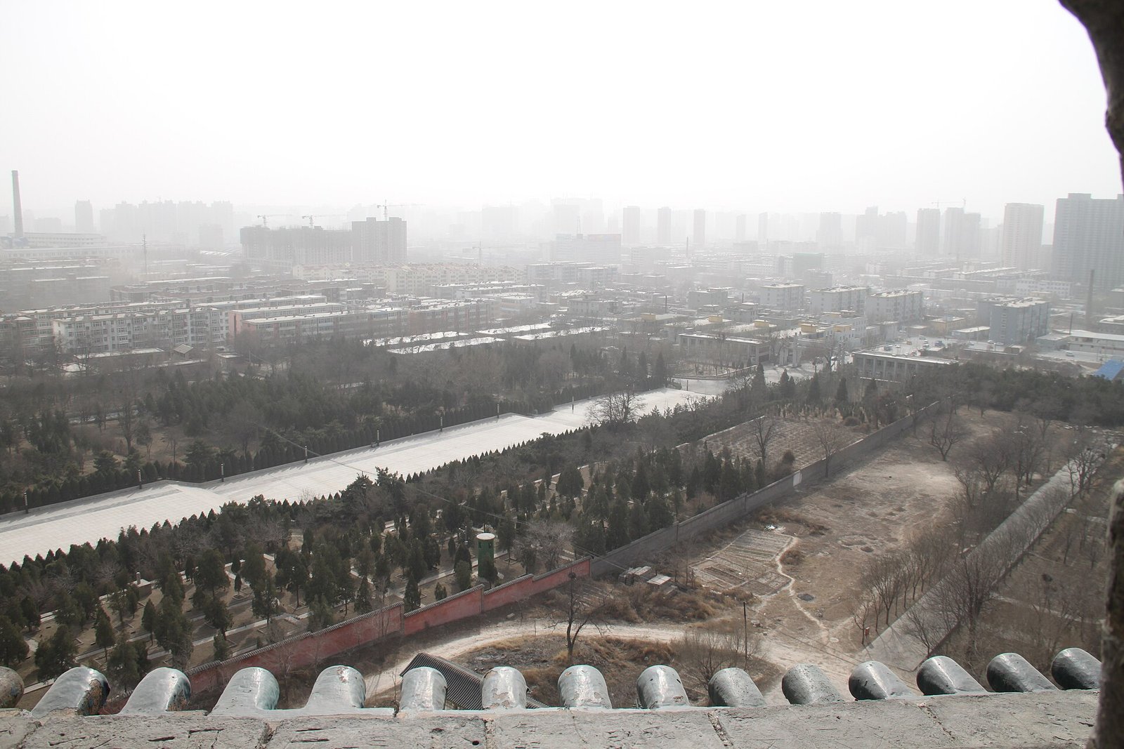 A hazy city view from a high vantage point, with low buildings, roads and distant mountains