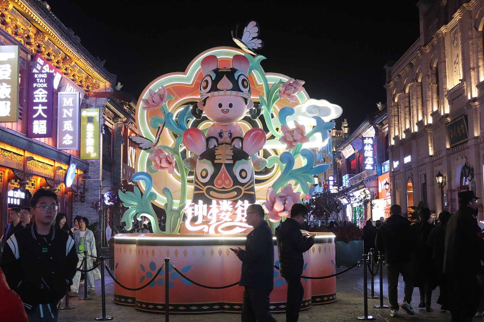 A pedestrian shopping street at dusk with lit facades in a 1920s commercial style and people walking