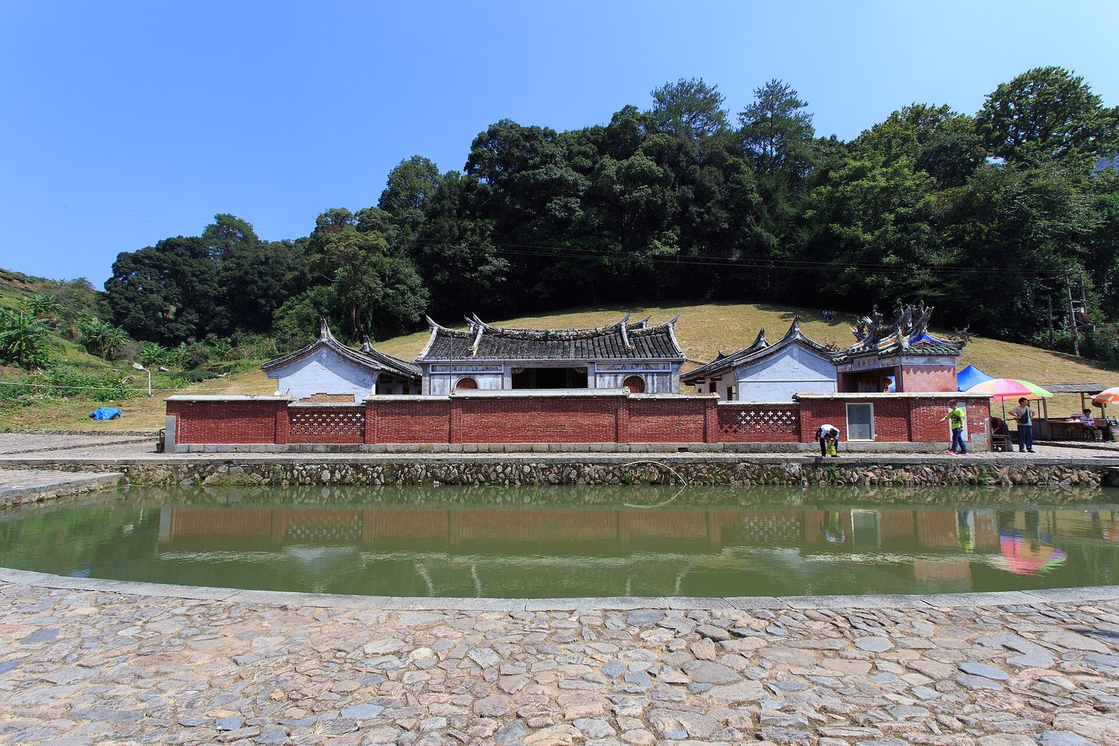 The Deyuan Tang ancestral hall at Taxia village, with a pond in front and stone flagpole shafts along the bank