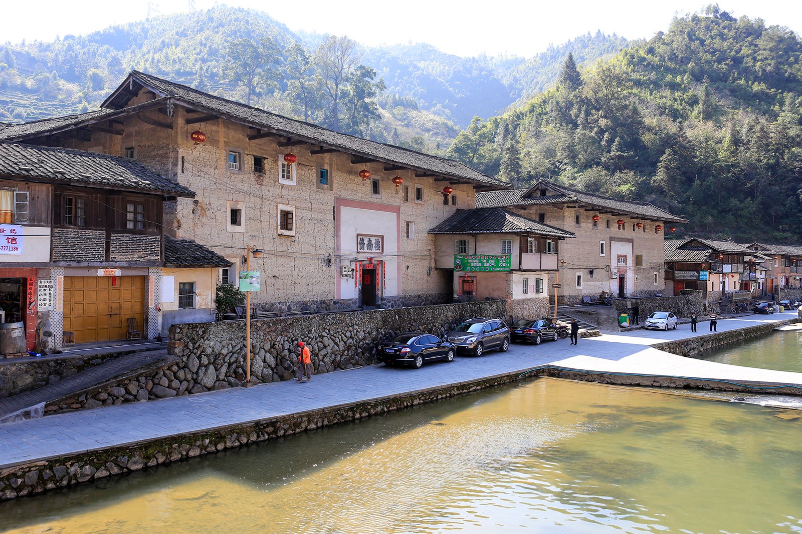 The village of Taxia with a pond in the foreground, low tiled buildings along the bank and wooded hills behind