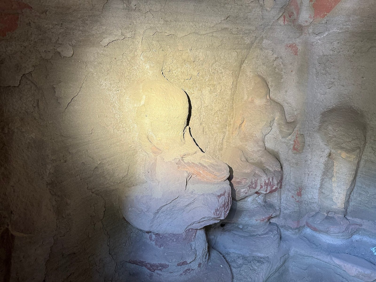 A carved Buddhist figure in a rock-cut cave, lit from the side, with traces of pigment on the stone