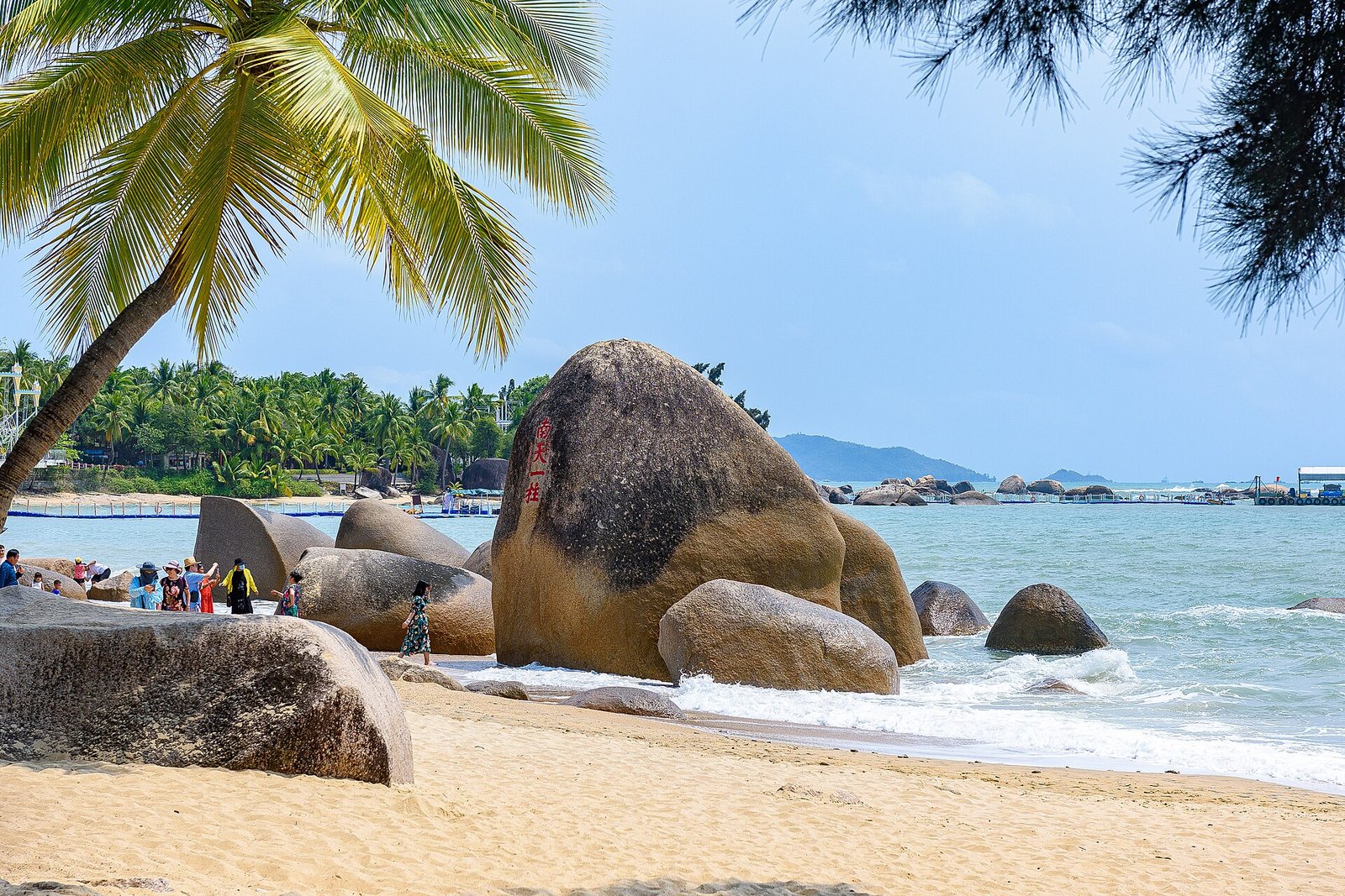 Two large rounded boulders on a sandy beach at Tianya Haijiao with palm fronds overhead