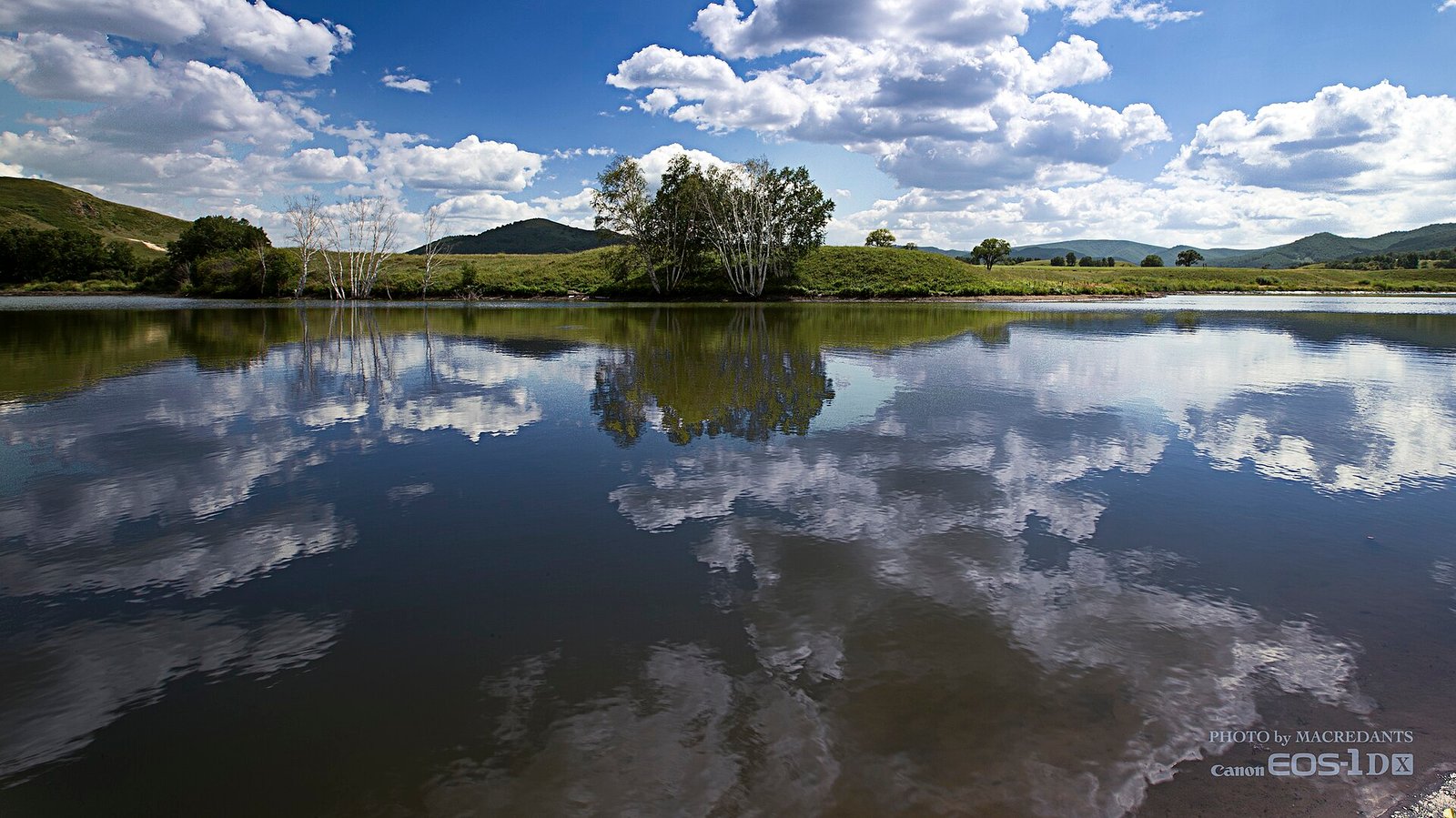A still lake reflecting cumulus cloud and a low grassy shore on the Hexigten grassland in Inner Mongolia