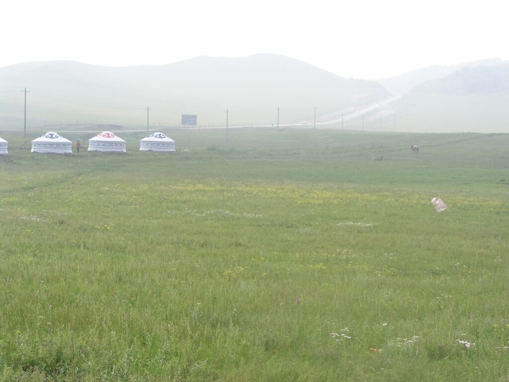 Yurts standing in mist on the grassland at Wulanbutong in Inner Mongolia, with hills fading behind