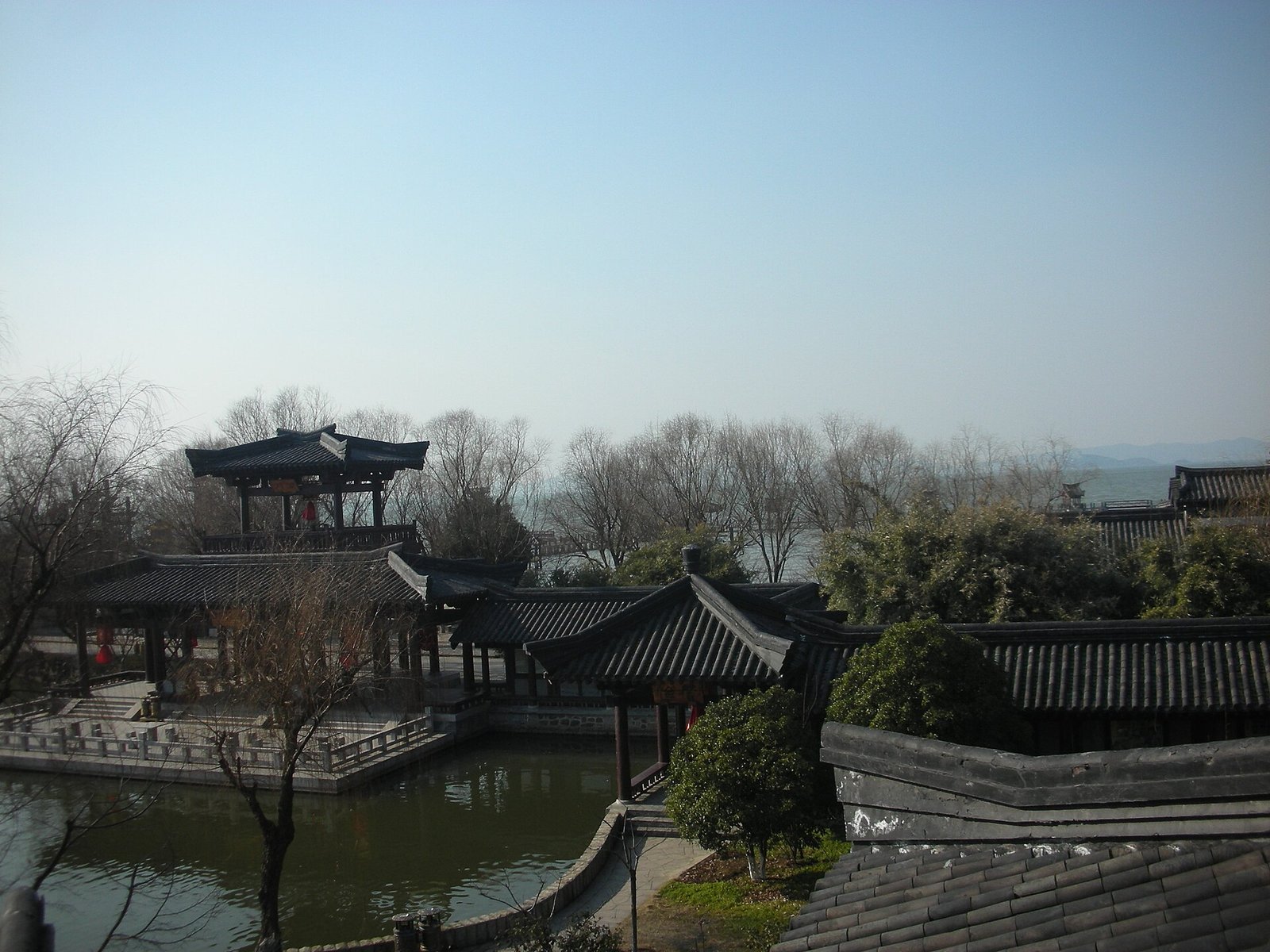 Classical Chinese pavilions and a pond at the Wuxi Three Kingdoms film set, with Lake Tai and hazy hills beyond