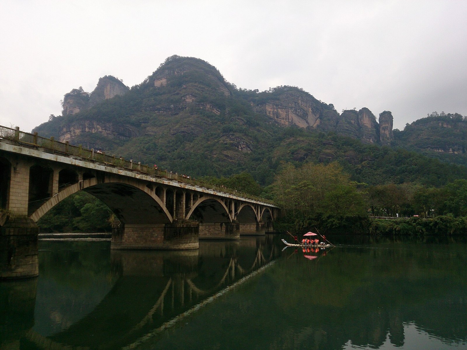 A bamboo raft with passengers passing beneath a concrete road bridge on the stream at Wuyishan