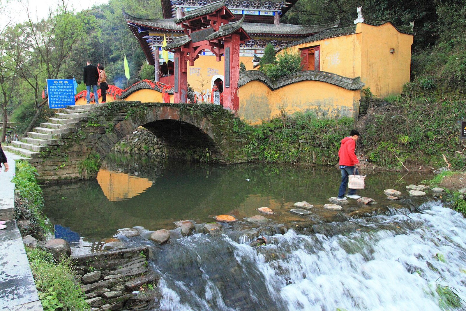 A stone bridge over a shallow stream at Likeng in Wuyuan, with a yellow-walled shrine behind