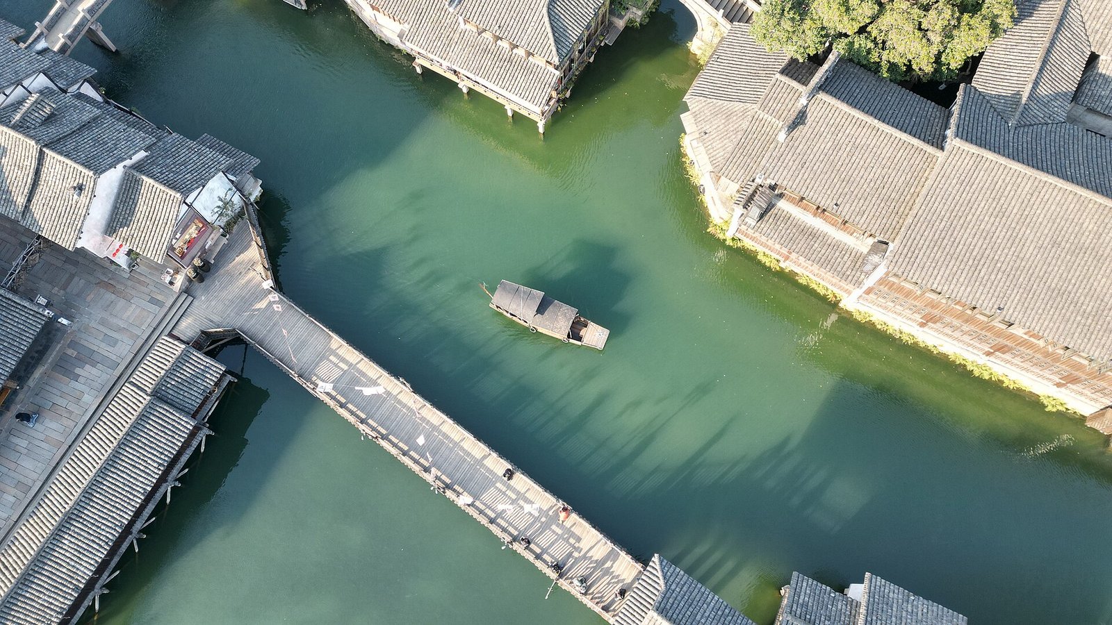 An aerial view looking down on a broad canal at Wuzhen with a long wooden boat and old buildings on both banks
