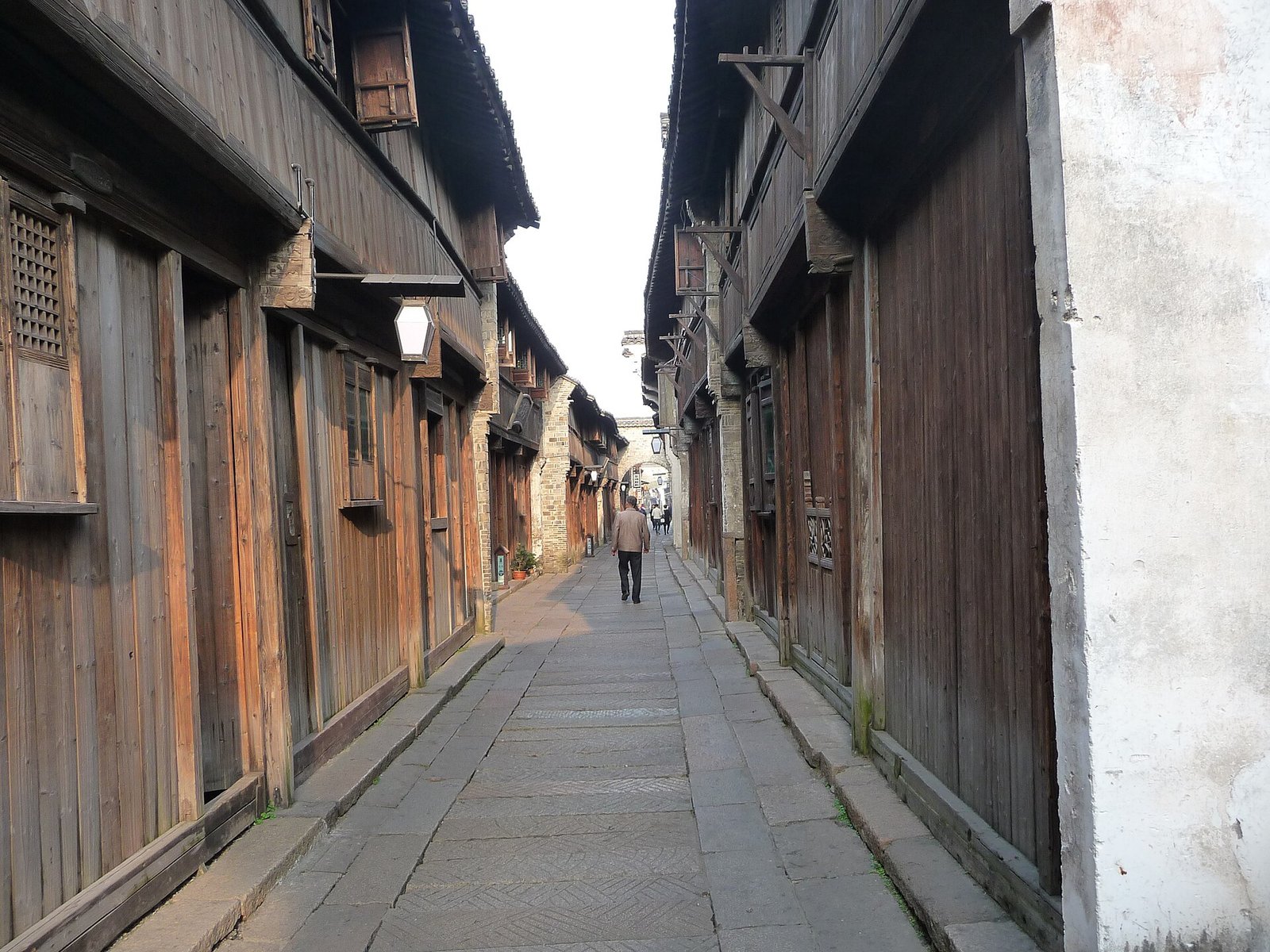 A narrow stone-paved alley between old wooden shopfronts in Wuzhen, with a doorway at the far end