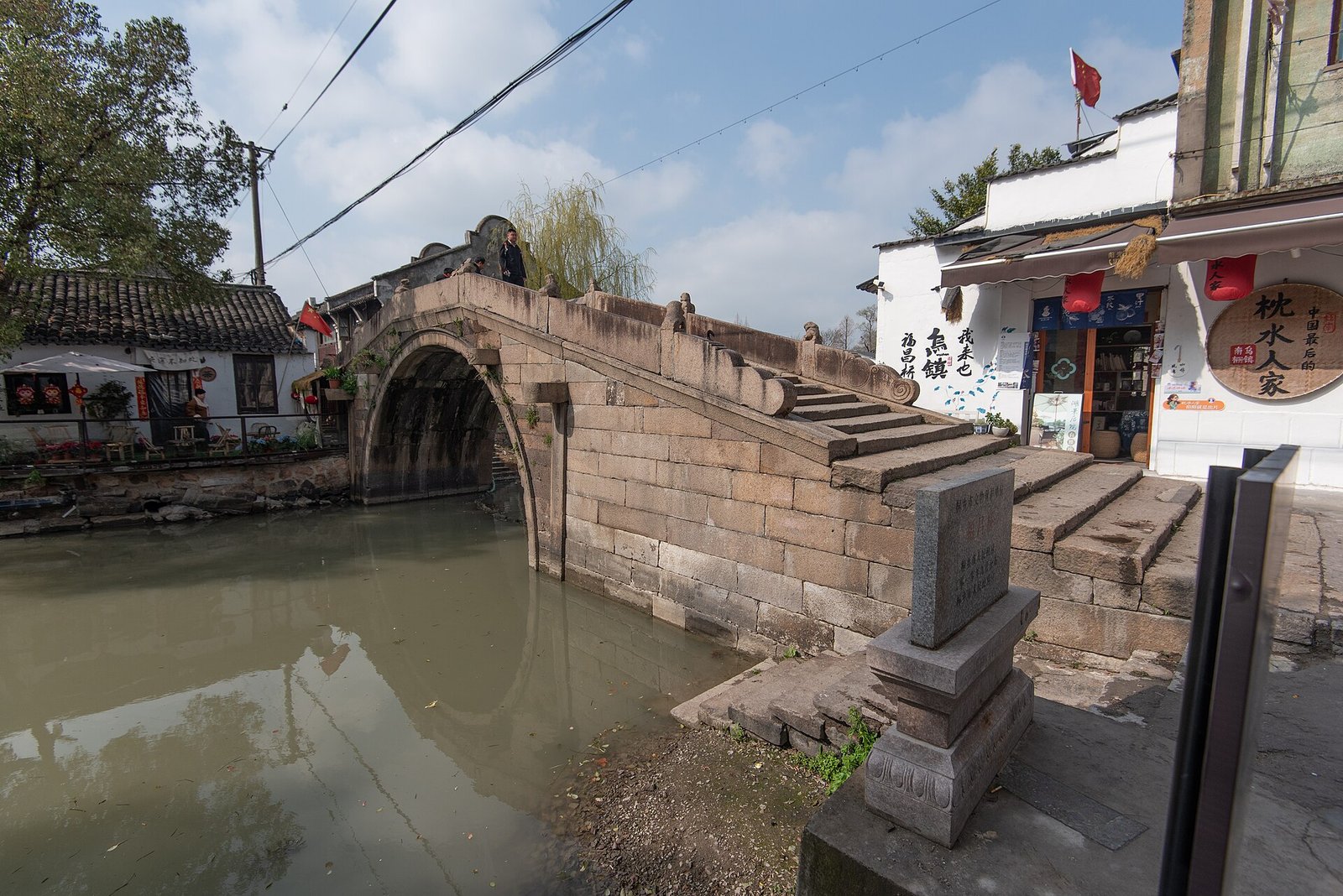 A weathered stone bridge over a canal in Wuzhen Nanzha, with old low houses and washing lines on the far bank