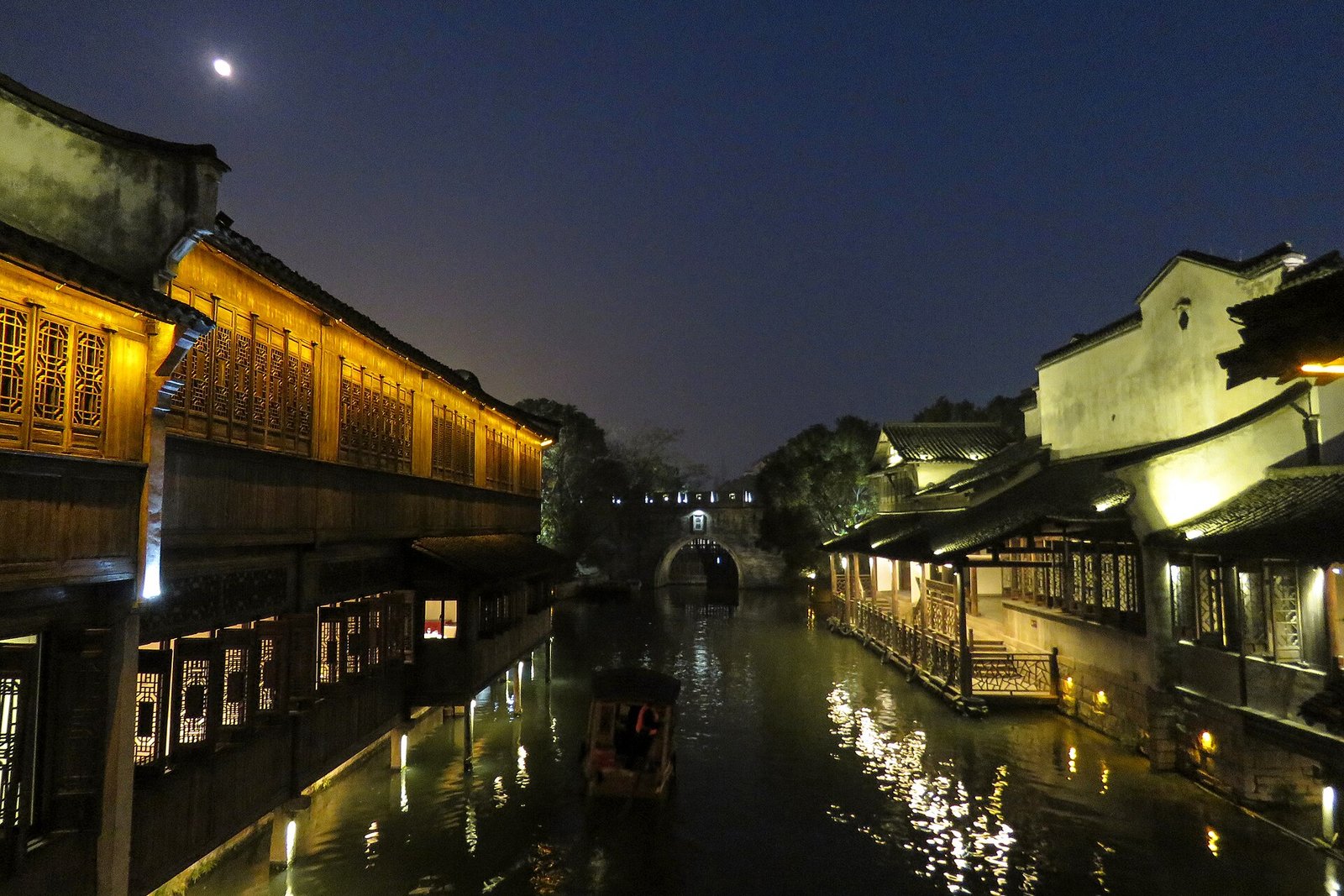 Lantern-lit houses along a canal at Wuzhen Xizha at night, with reflections in the still water and a dark blue sky above