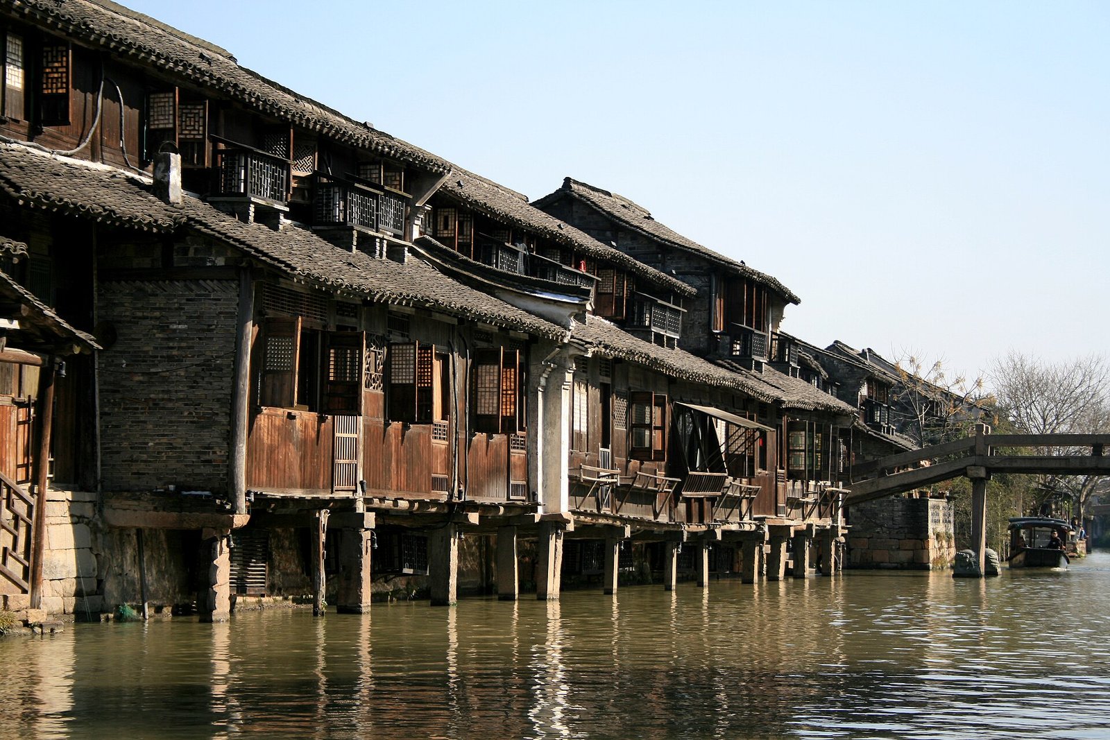 Timber water pavilions built out over a canal on stilts at Wuzhen, with boats moored underneath