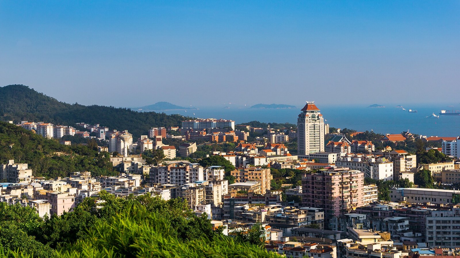A wide view over the Xiamen University campus and the surrounding hillside city, looking toward the sea