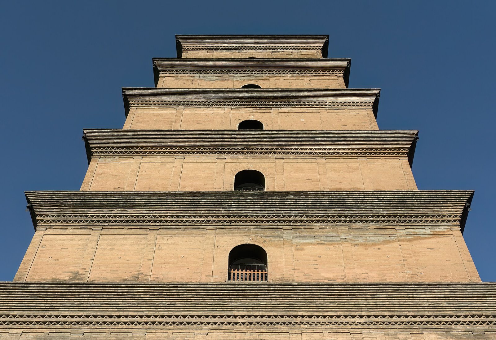 A tall, tapering brick pagoda seen from below against a clear blue sky