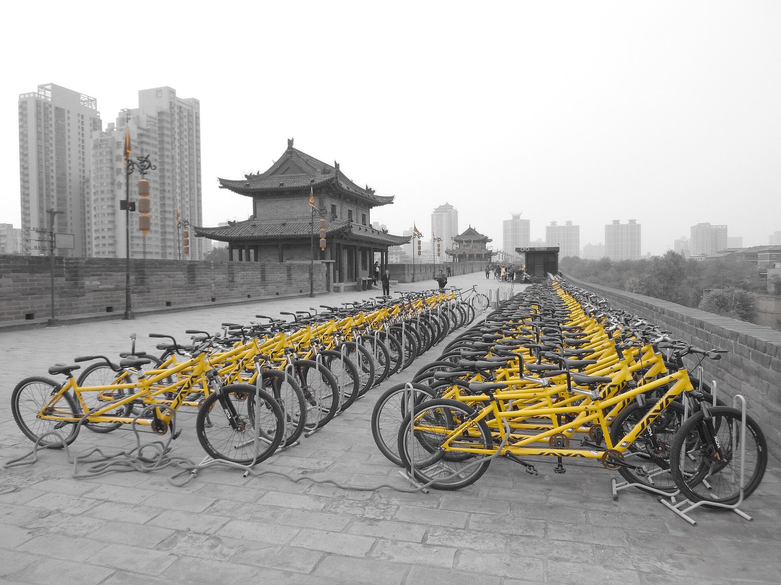 Rows of yellow bicycles parked on the wide paved top of an ancient city wall, with a gate tower and modern skyline behind