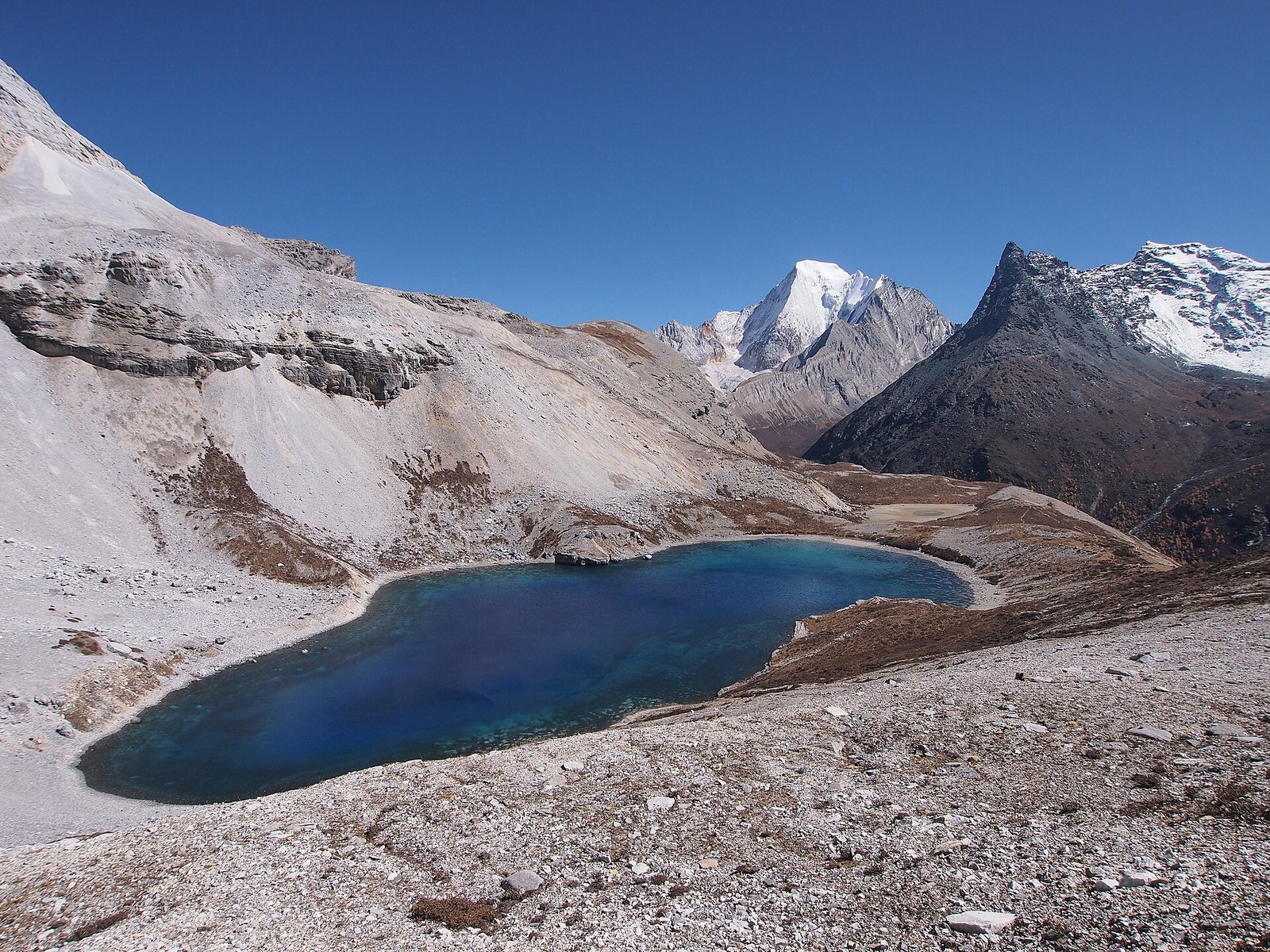 Five Colour Lake at Yading, a dark blue lake set in grey scree below a snow ridge