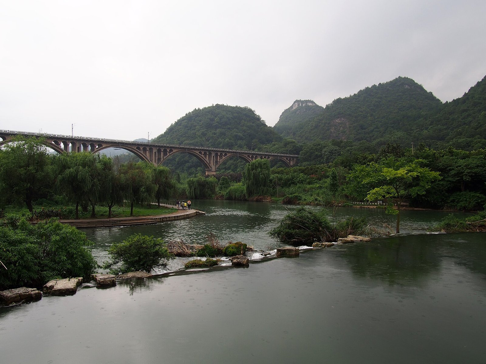 A stone-arch railway bridge crossing a green river between forested hills in Yunnan
