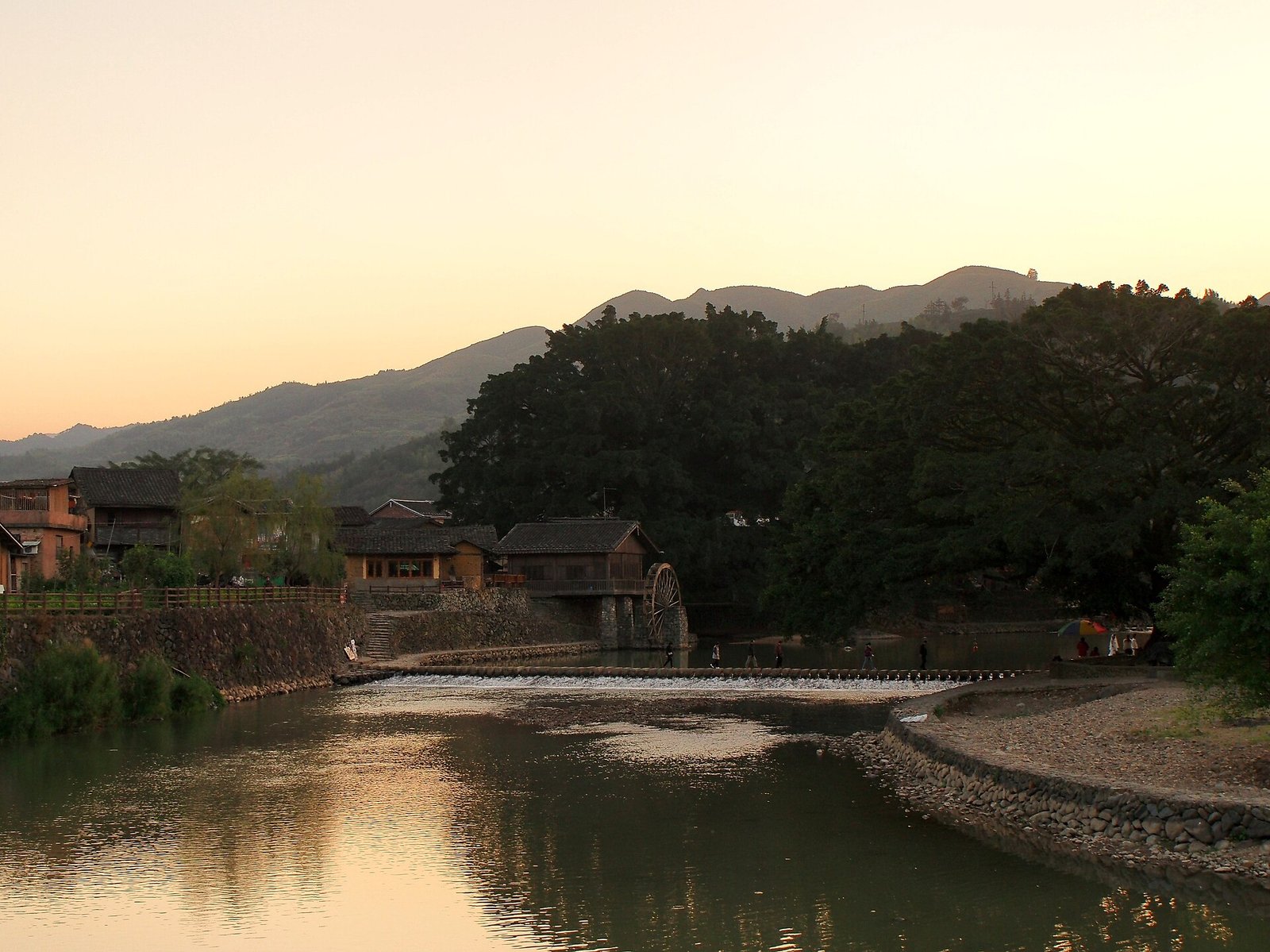 Golden evening light on the stream and stone bridge at Yunshuiyao village, with tulou and wooded hills behind