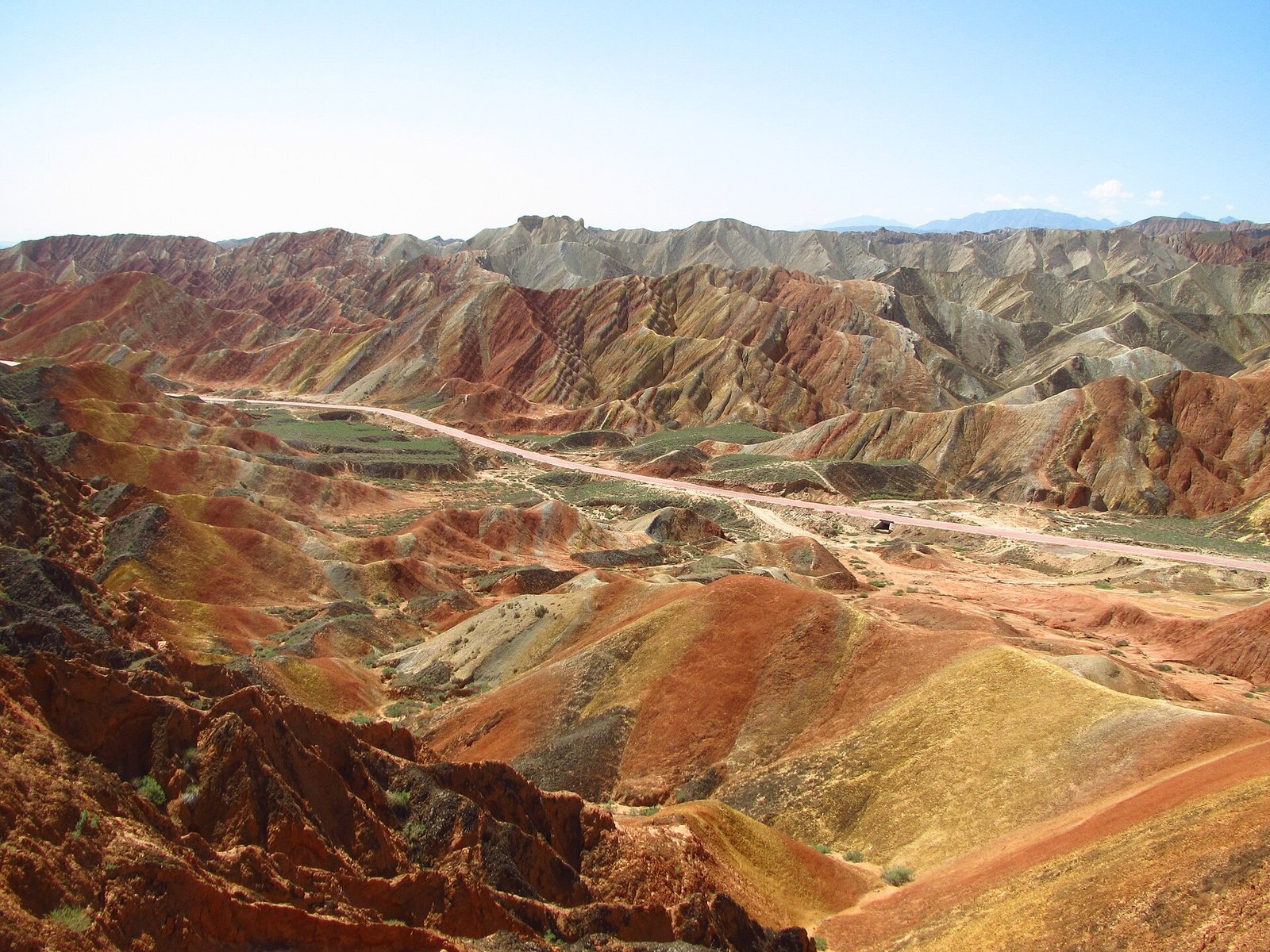 A wide view across the floor of the Zhangye Danxia scenic area with the access road running through and banded hills on both sides