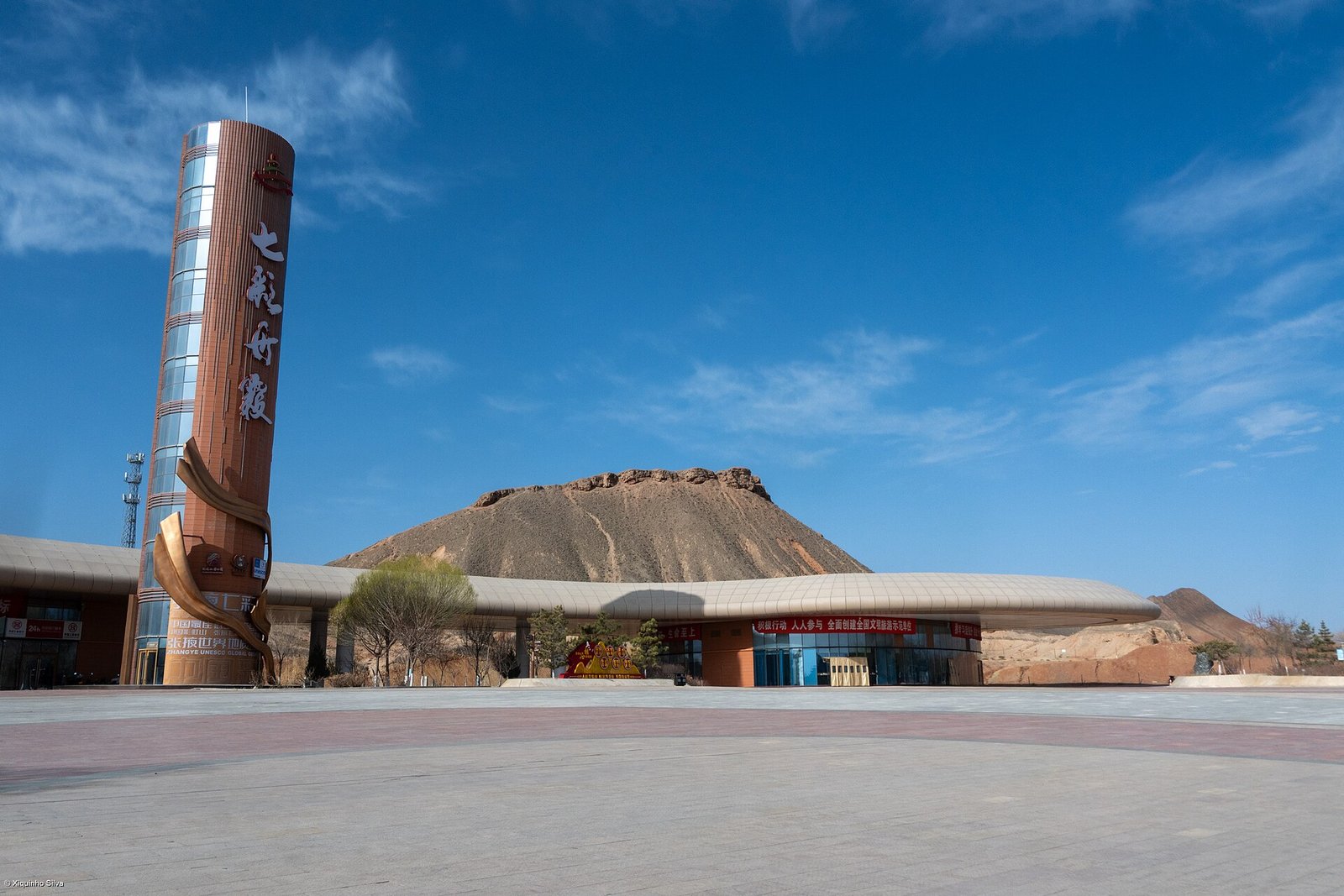 The visitor centre at the north gate of the Zhangye Danxia scenic area, a low modern building with a tall tower, under a clear blue sky