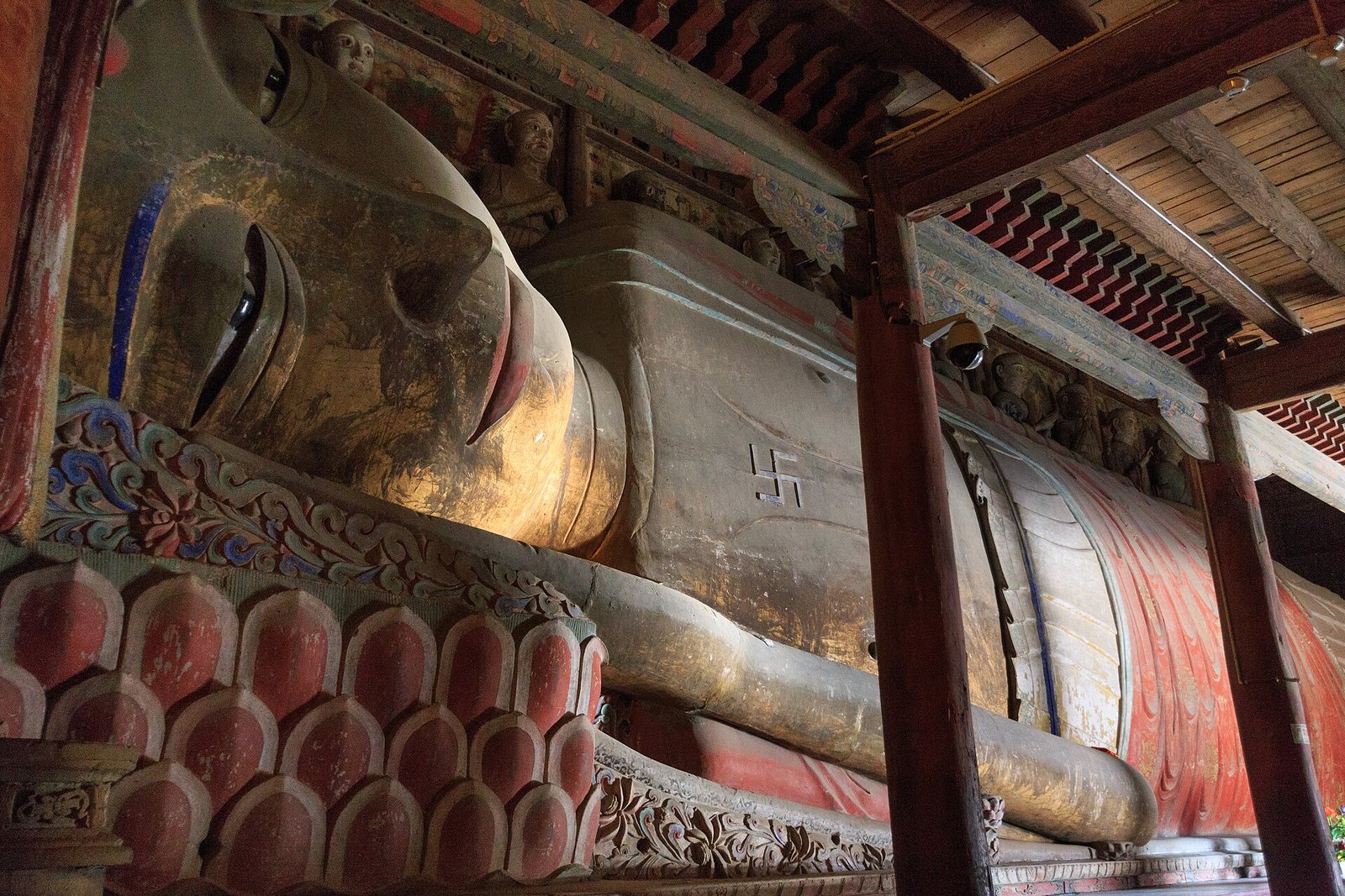 The giant reclining Buddha inside the Grand Buddha Hall at Zhangye, seen from the side with painted beams and red pillars above