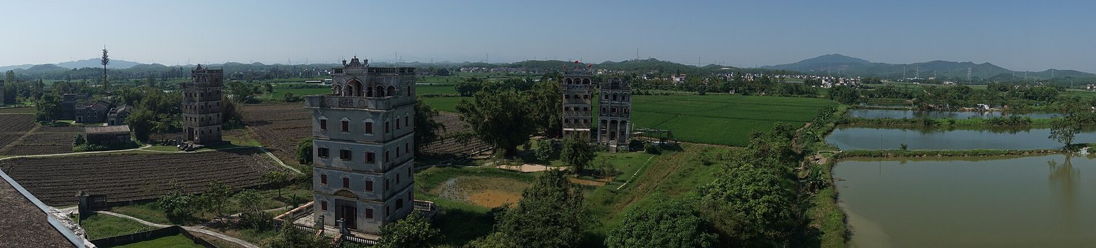 A wide panoramic view of rice fields with several fortified towers standing along the far edge